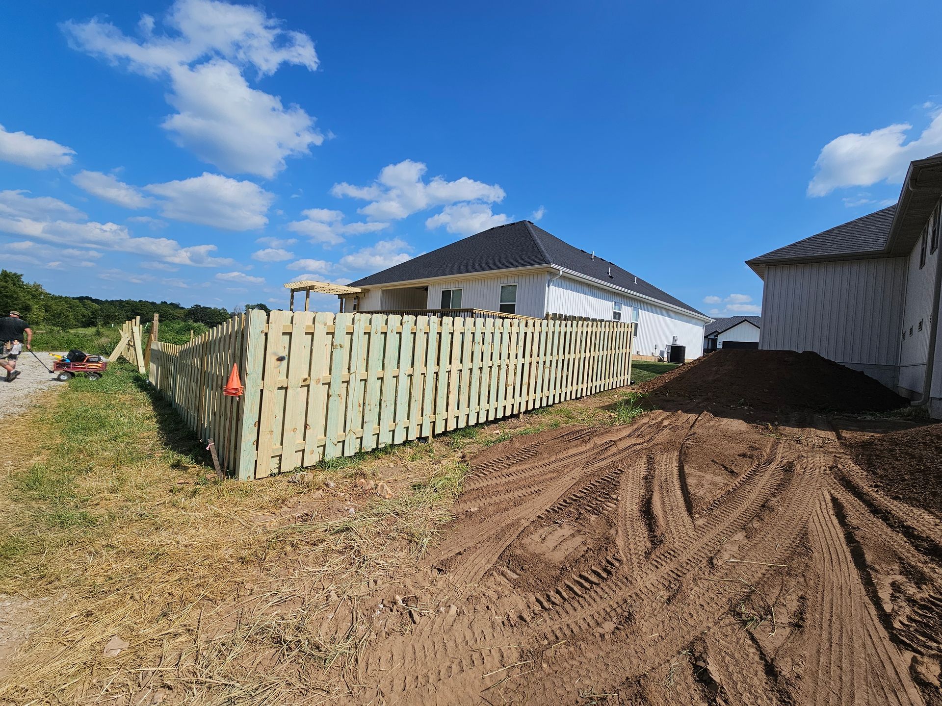 A newly built house with a wooden fence in a construction site under a blue sky.