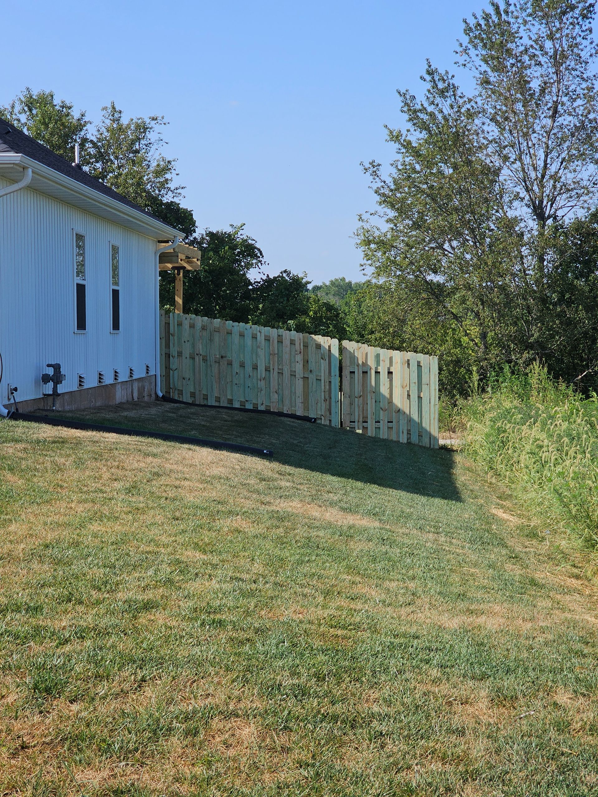 Wooden fence next to a white house and grassy yard.
