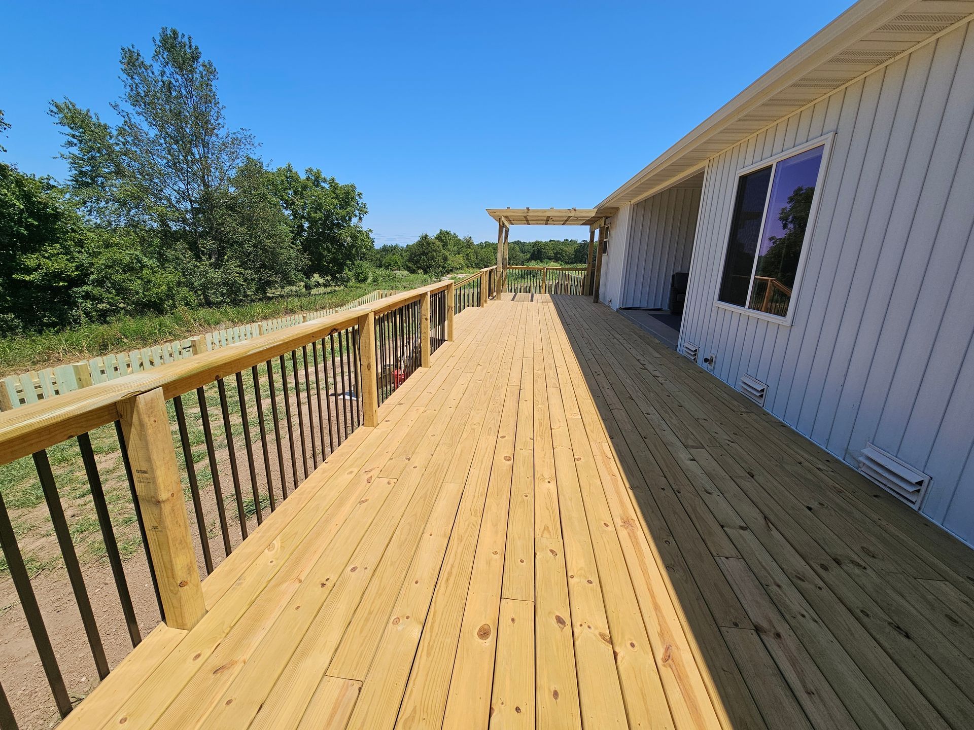 Wooden deck with black railings and a white house, under a clear blue sky.