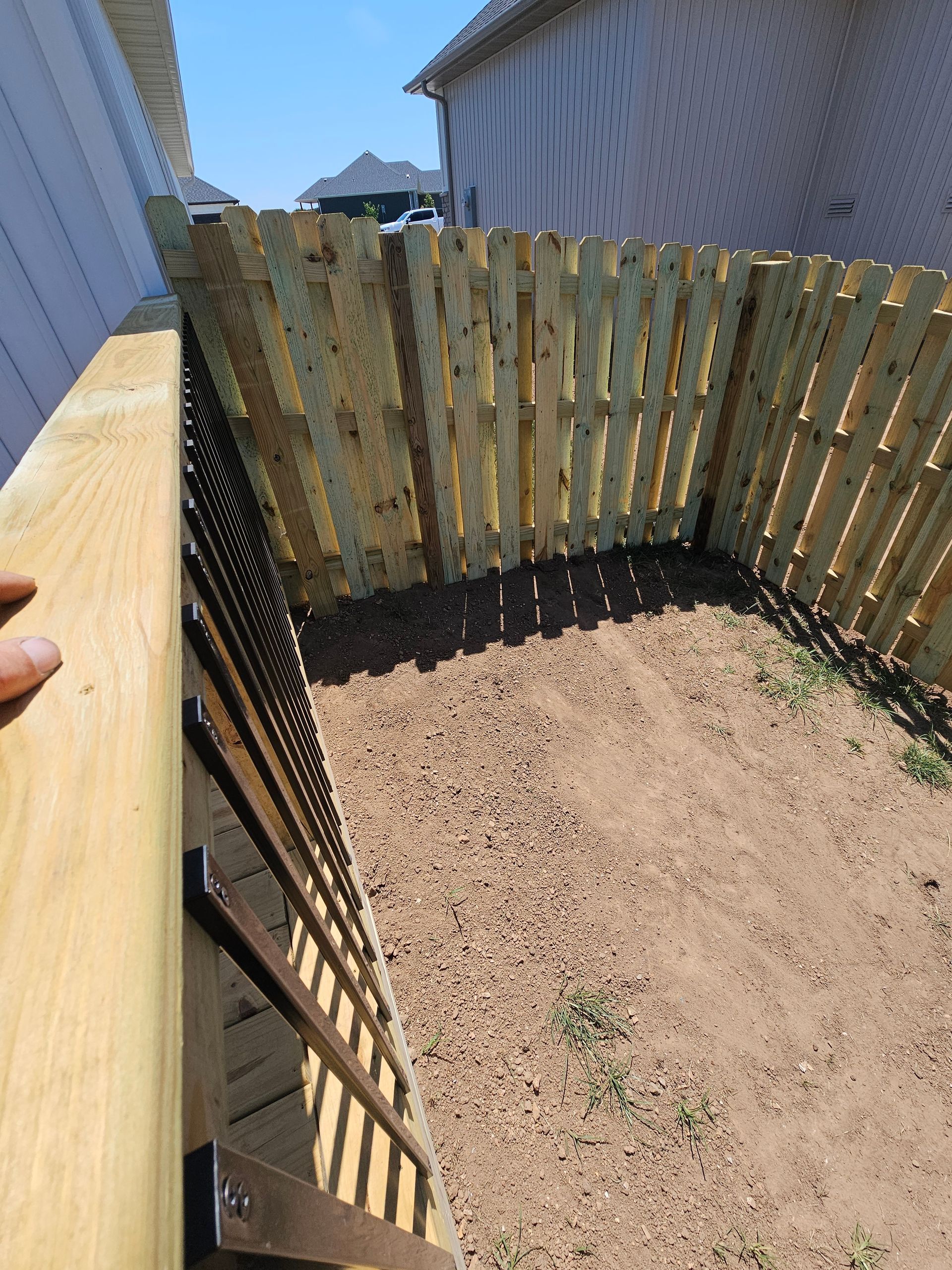 Wooden fence and deck enclosure with gravel ground; sunny outdoor setting.