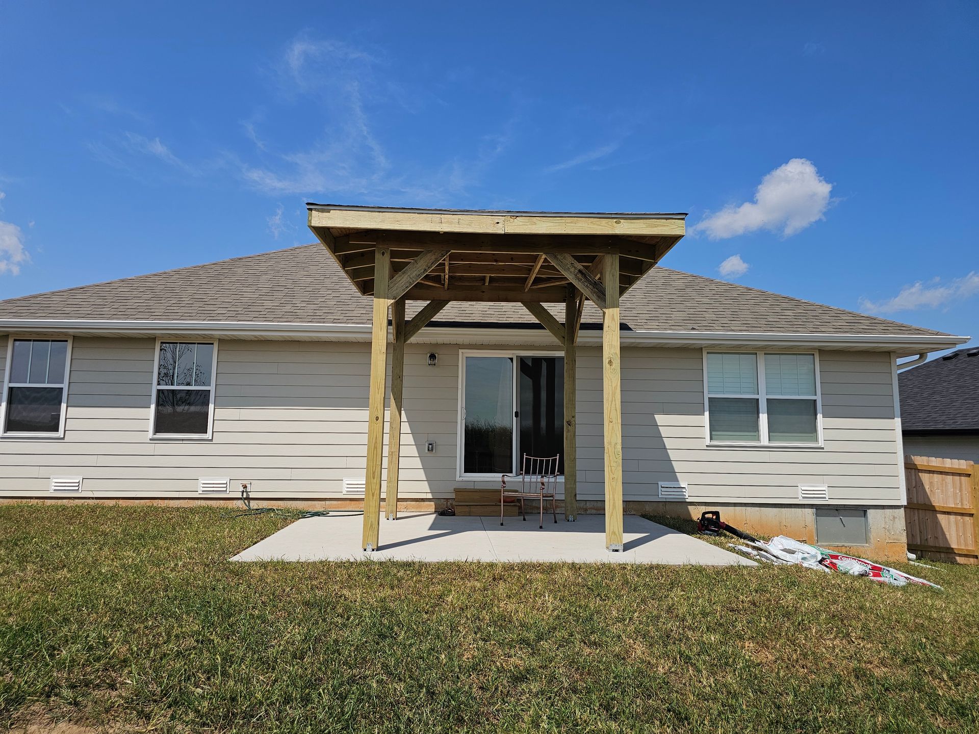 Backyard view of a house with a newly constructed wooden pergola over a concrete patio.