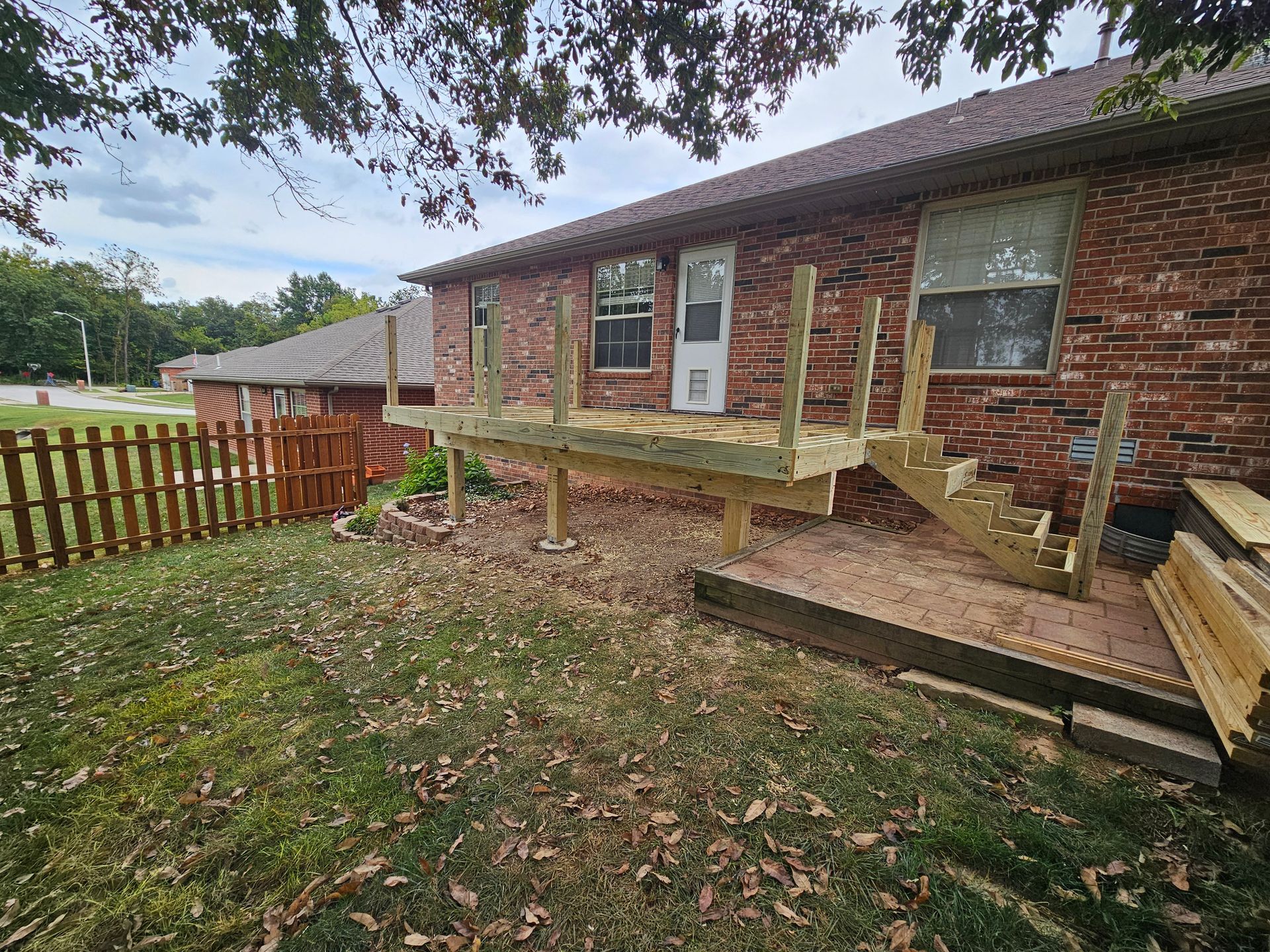 Newly constructed wooden deck with steps attached to a brick house. A brown fence is on the left.