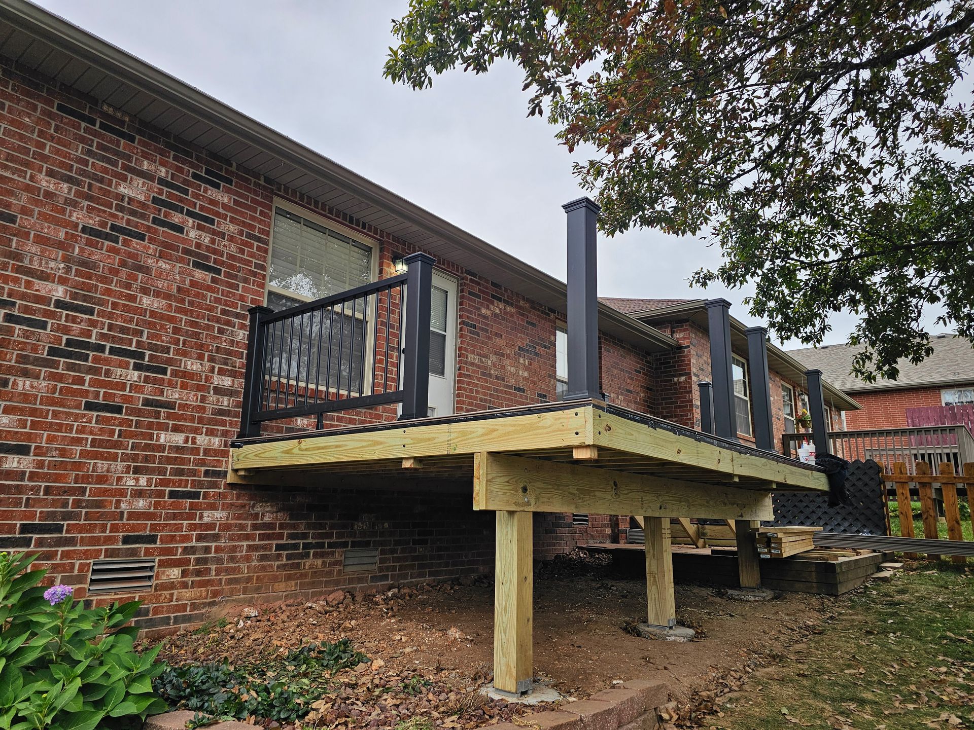 Newly constructed wooden deck with black railing against a brick house.