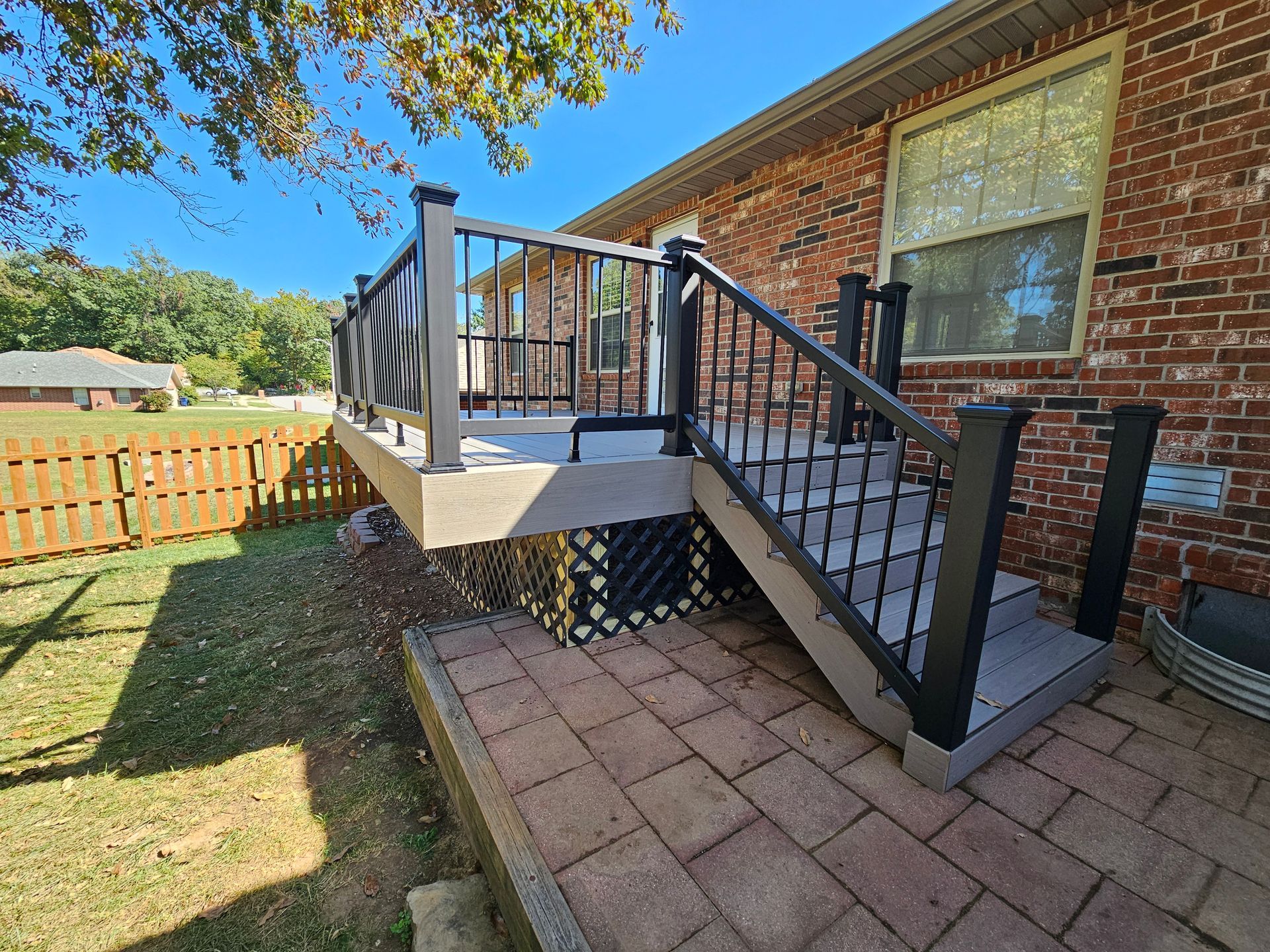 Deck with stairs, brick house background, brown and black railing, sunny day.