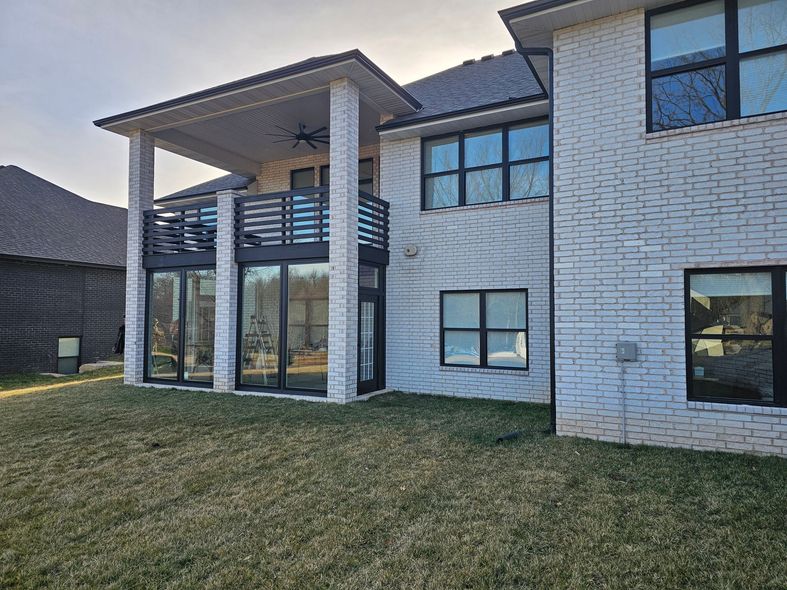 Back of a white brick house with a covered patio, balcony, and dark-framed windows.