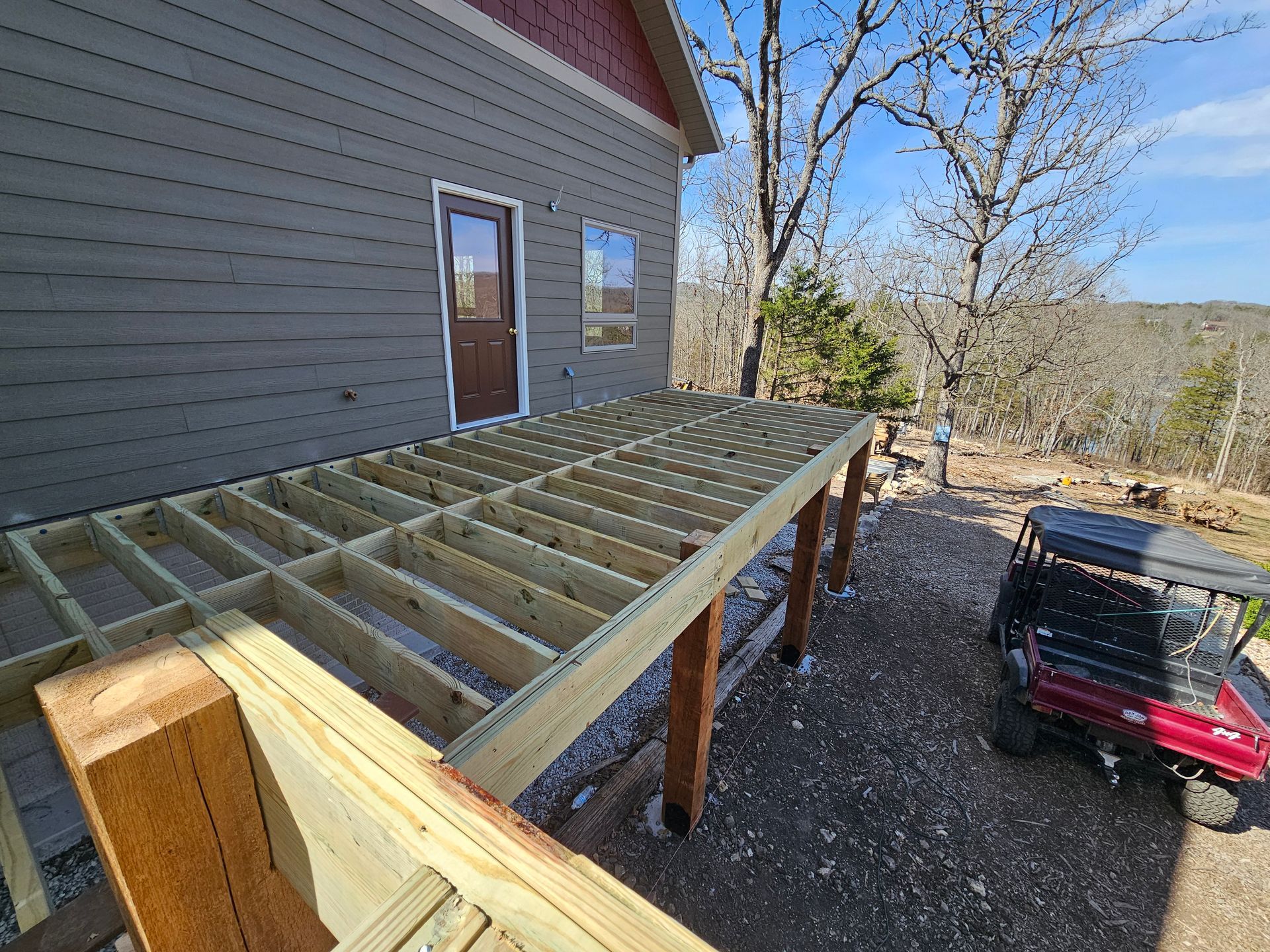 Wooden deck under construction next to a house with an open doorway. A red golf cart sits nearby.