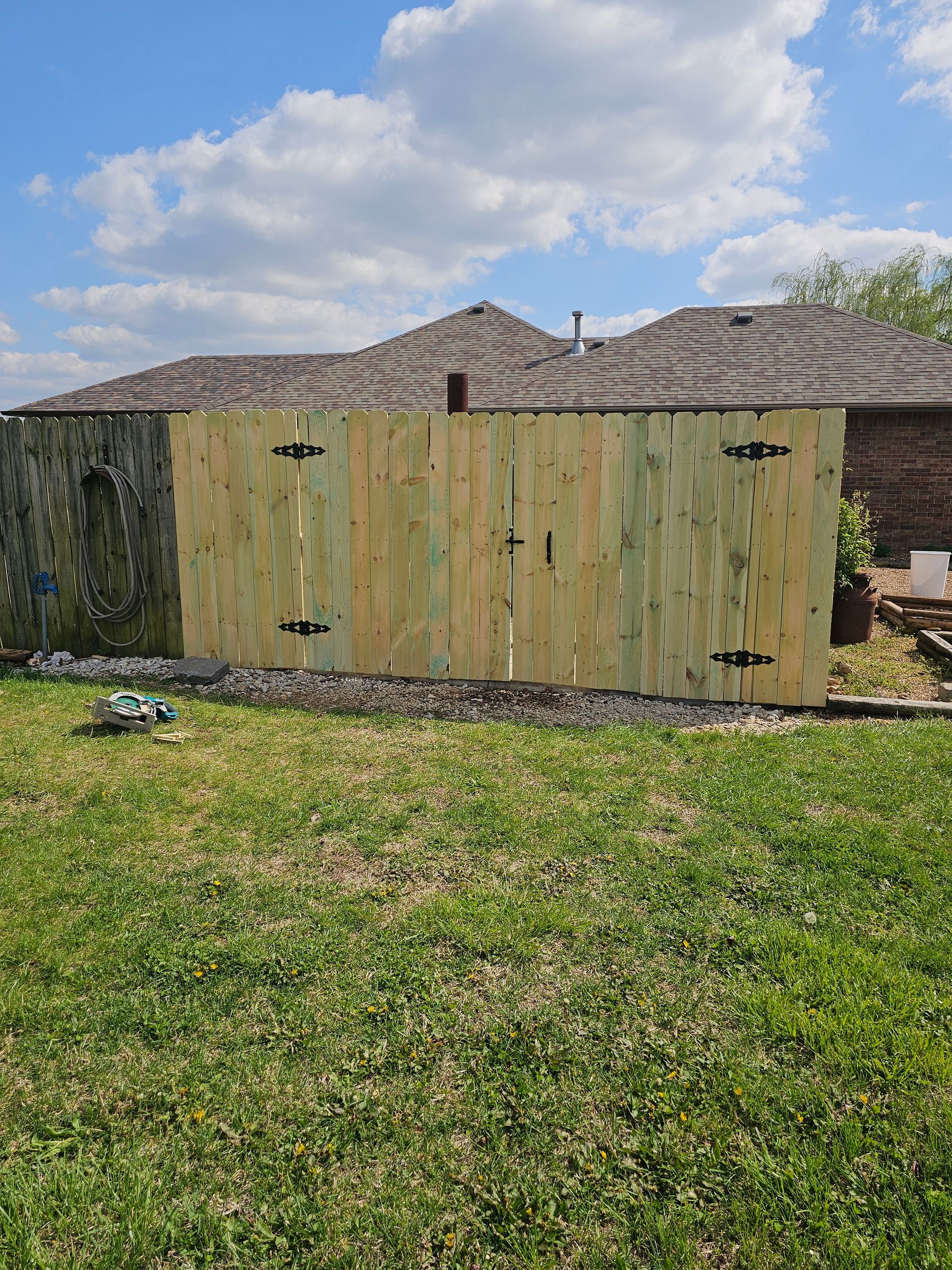 Wooden fence with a gate in a grassy backyard under a partly cloudy sky.