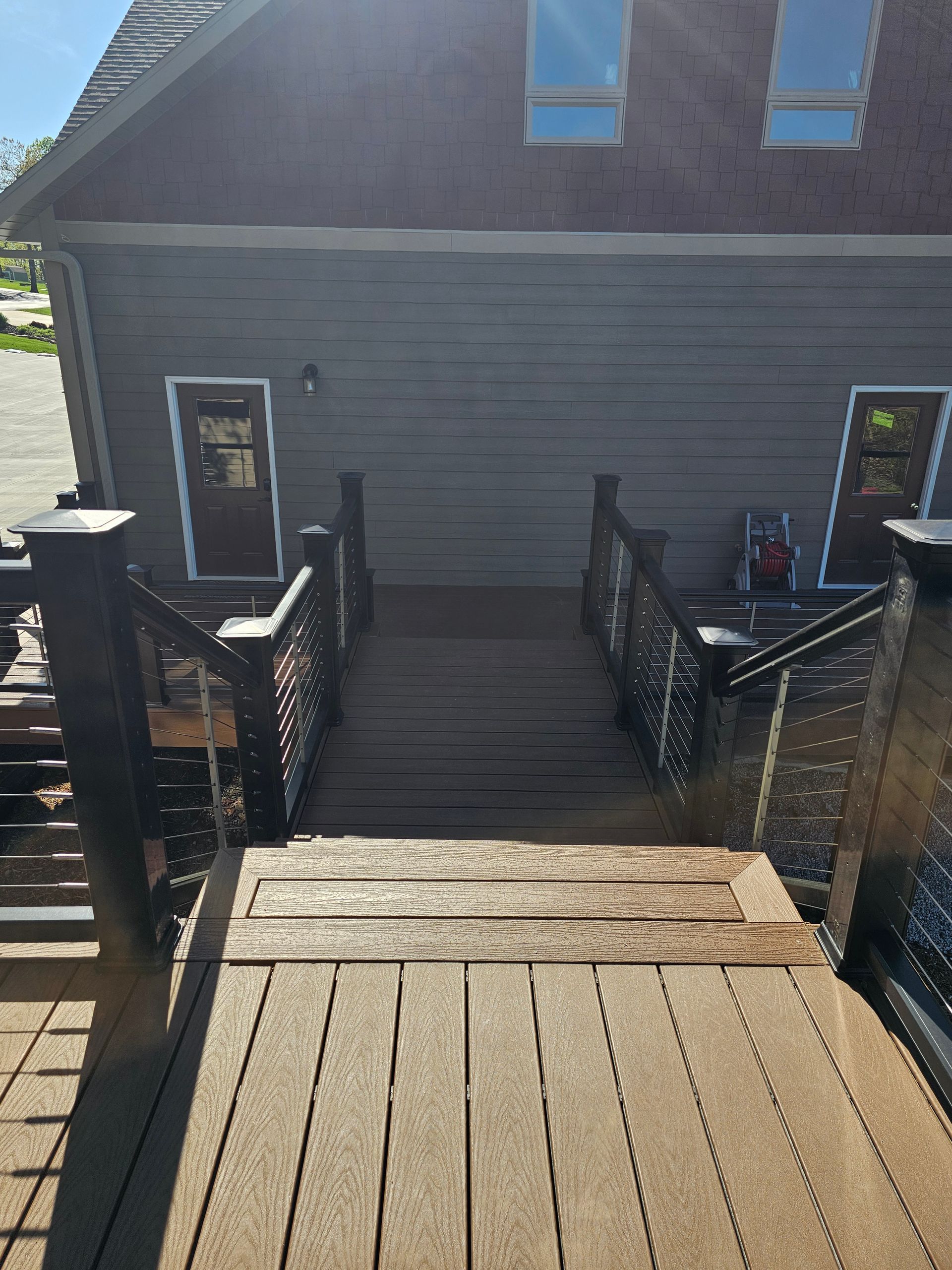 Wooden deck with stairs leading to doors on a building, railings on either side.