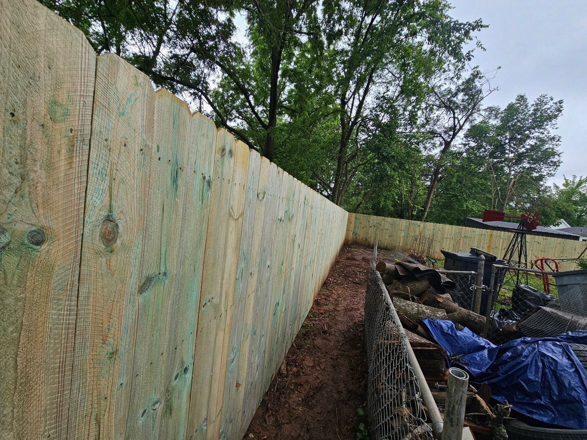 Wooden fence with a slight incline, with dirt and debris below, and trees in the background.