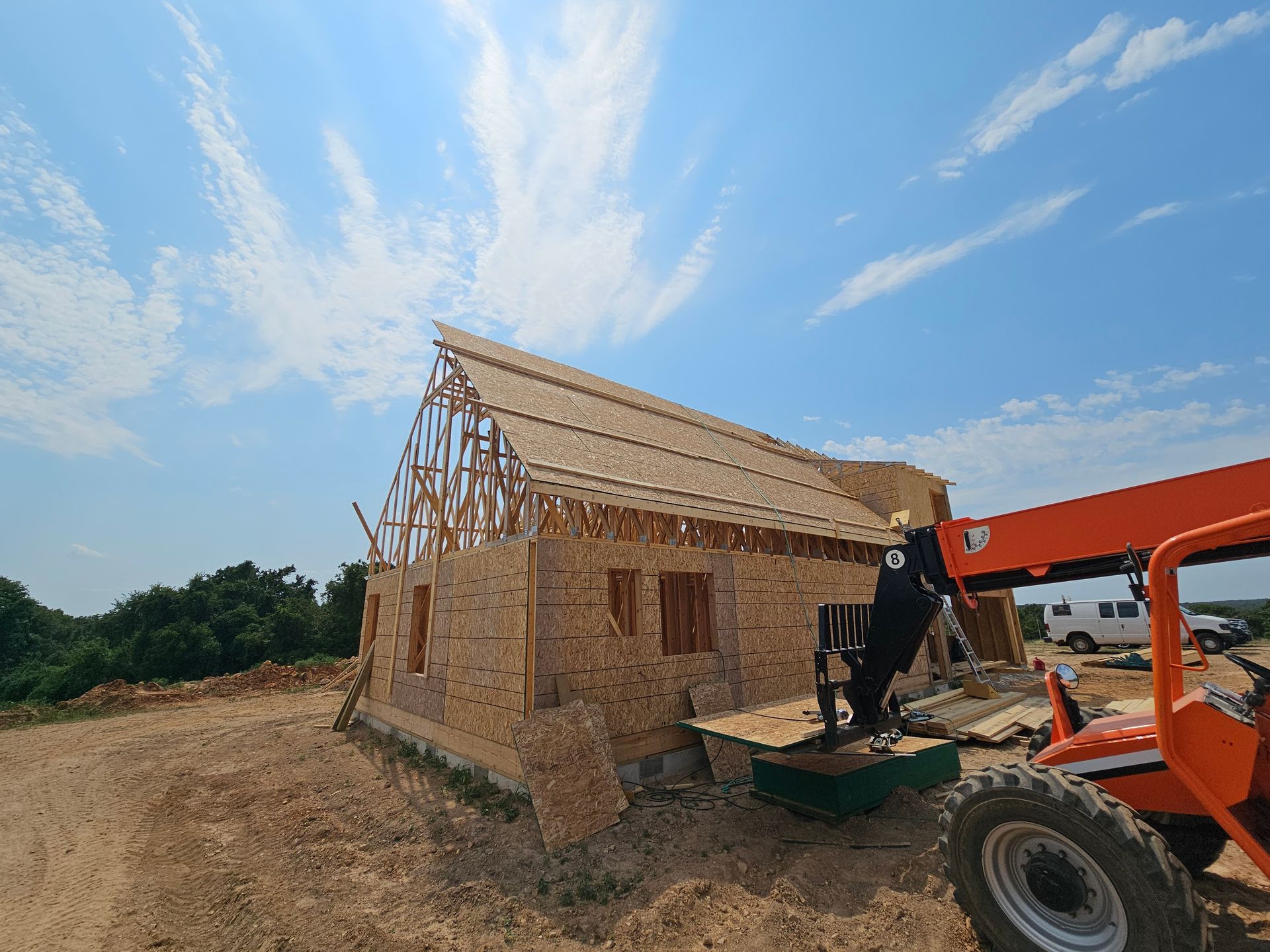 Construction of a wood-framed house under a blue sky, with an orange lift in the foreground.