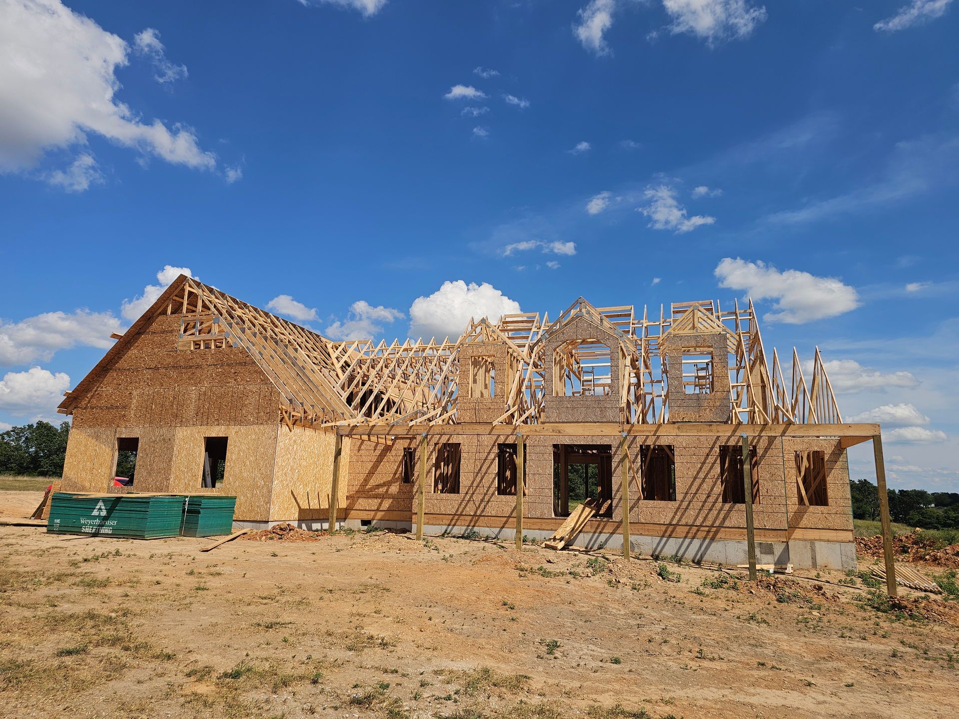 House under construction with exposed wooden frame against a blue sky with clouds.
