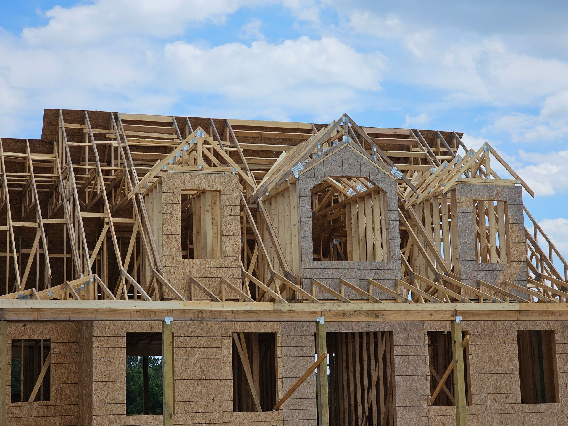 House under construction; wooden frame, open windows, dormers, blue sky background.