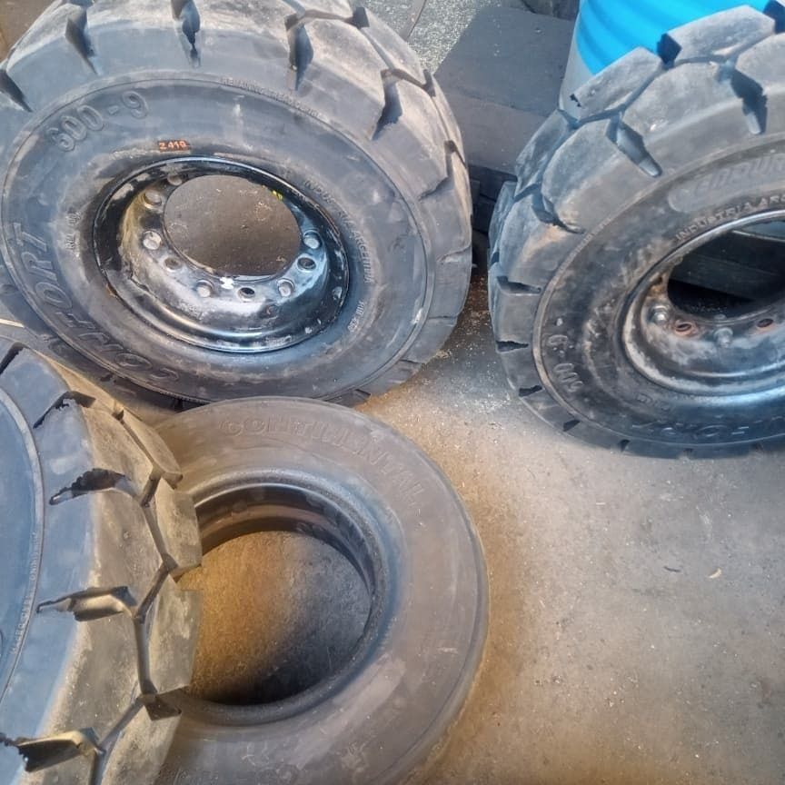 Cuatro neumáticos industriales grandes y negros apilados sobre un piso de concreto, con banda de rodadura visible y llantas de metal.