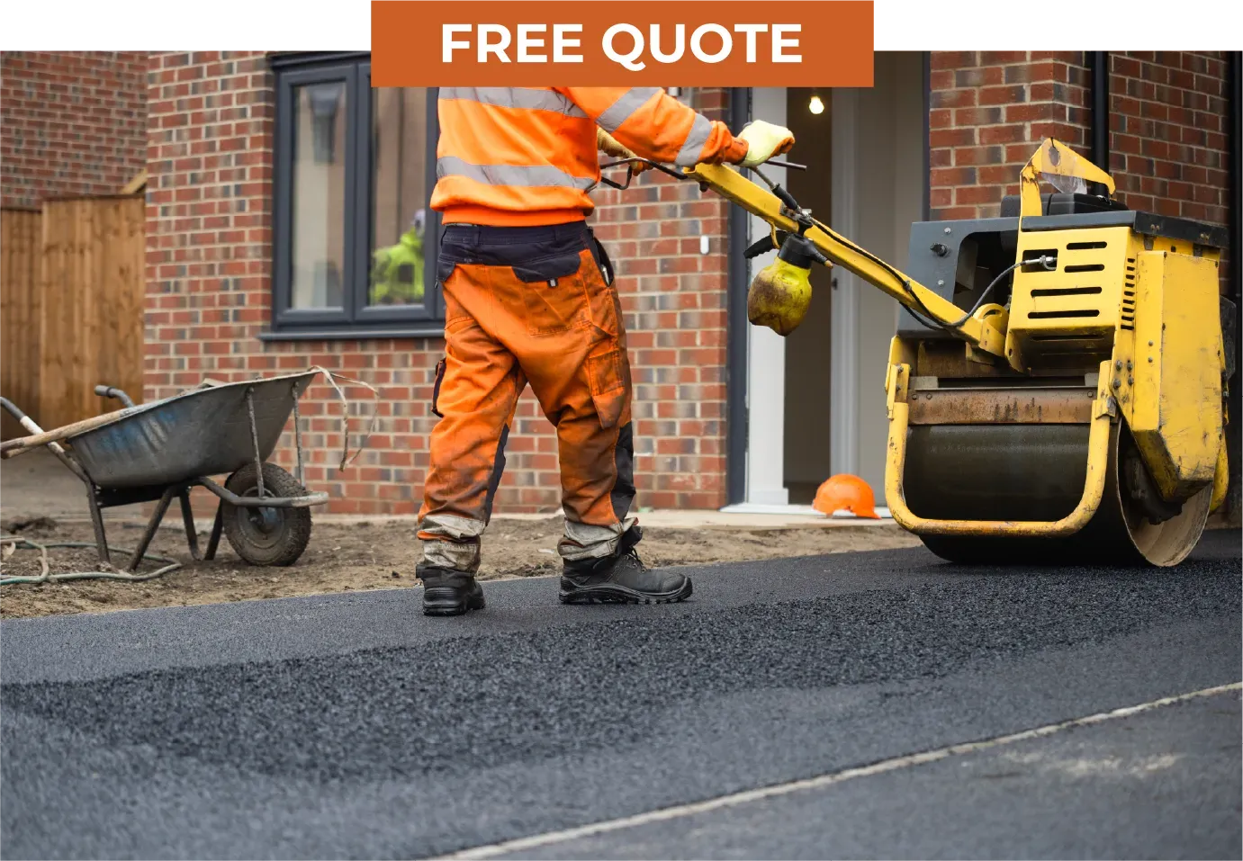 A worker in high-visibility orange clothing uses a yellow asphalt roller to compact a driveway in front of a brick house.