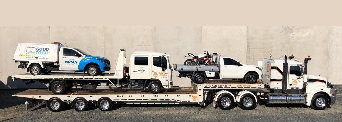 2 Tow trucks are parked alongside a large concrete wall towing 2 utes — Coffs Auto Service in North Boambee Valley, NSW