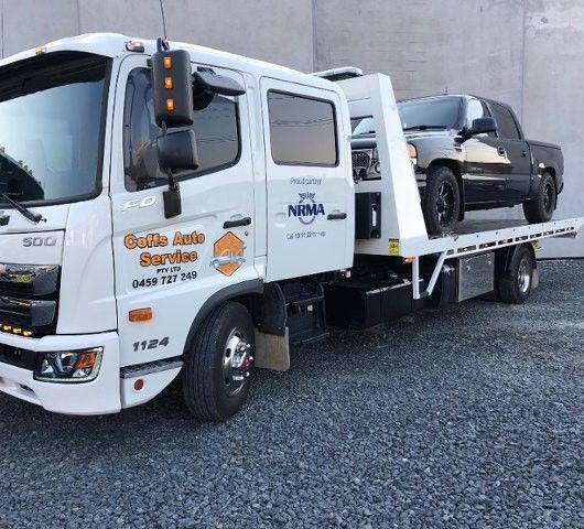 A Tow Truck With a Car on the Back is Parked in a Gravel Lot — Coffs Auto Service in North Boambee Valley, NSW