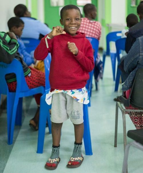 A young boy in a red sweater and grey shorts is standing in front of blue chairs