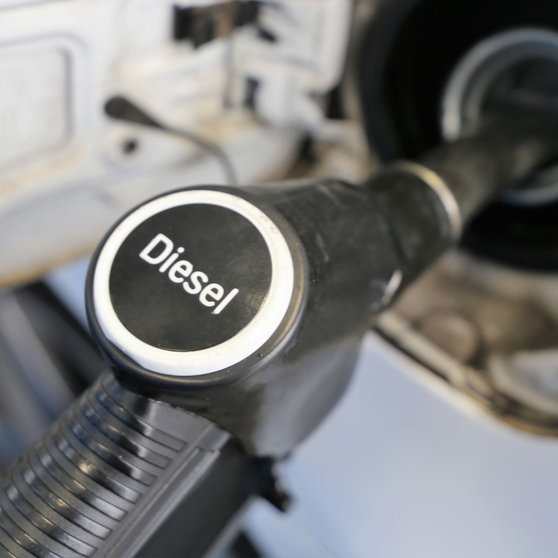 A black diesel fuel nozzle is inserted into a vehicle's open fuel tank.
