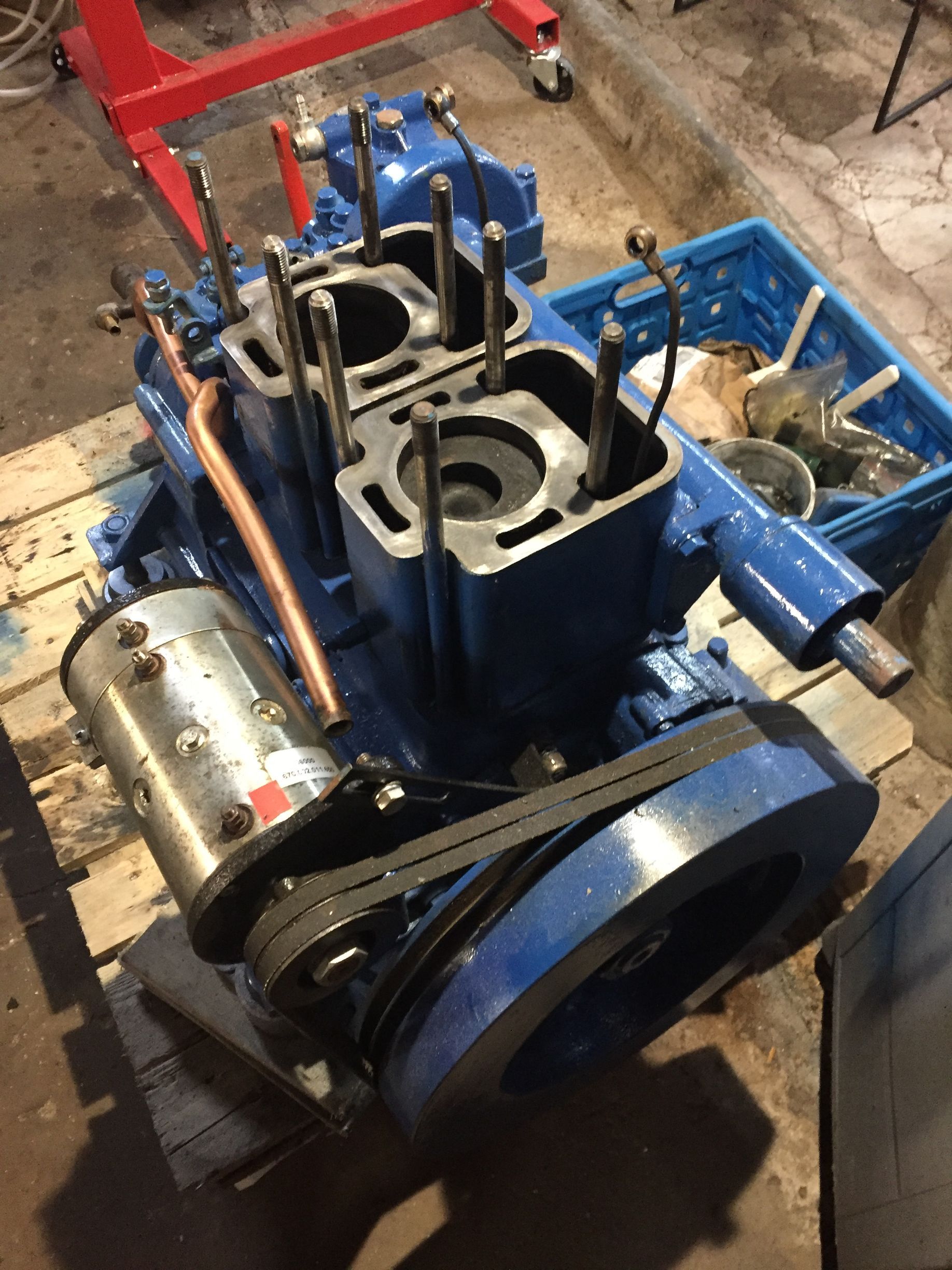 A blue engine is sitting on a wooden pallet in a garage.