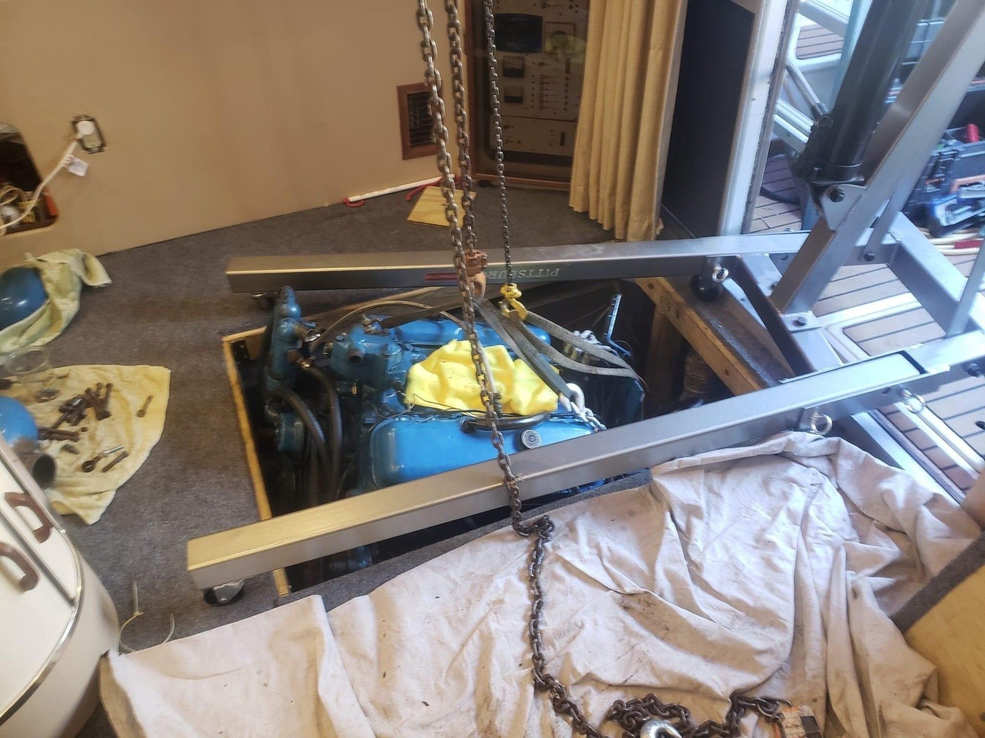 a boat engine hanging on chains from a engine crane being lowered into an engine room