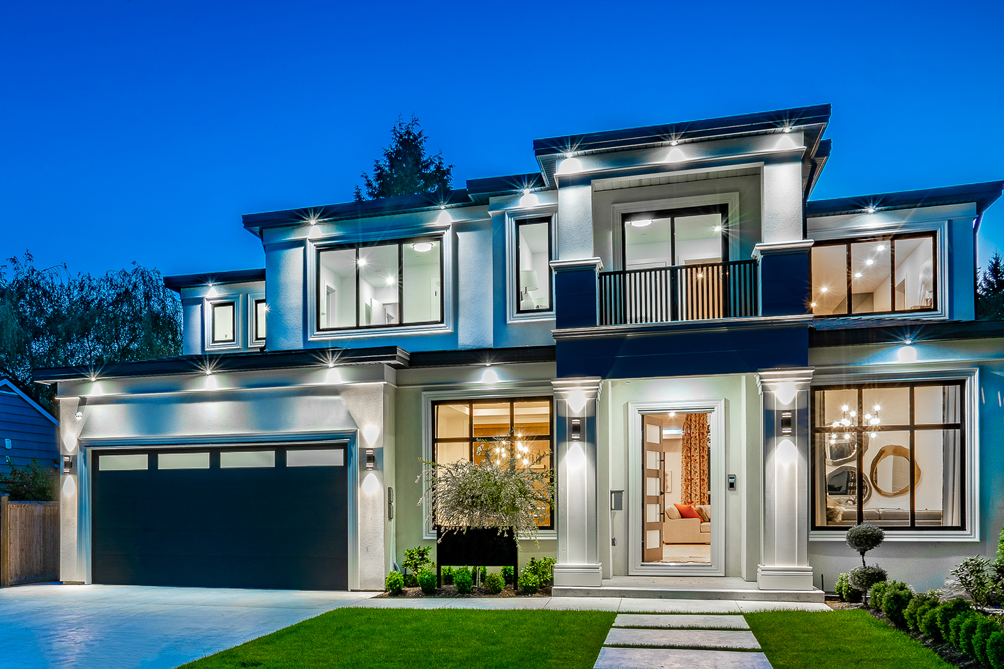 A large white house with a black garage door is lit up at night.