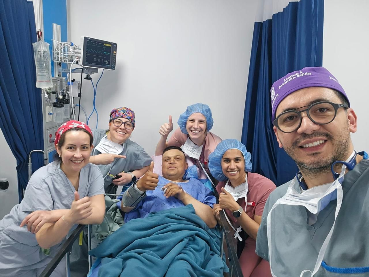 Personal médico y paciente sonriendo, dando pulgares hacia arriba en una habitación de hospital.