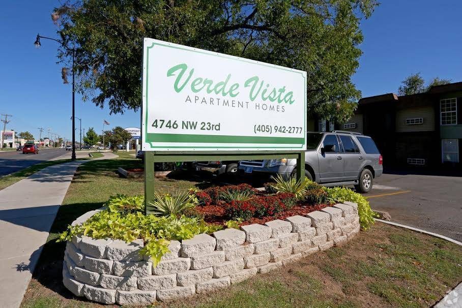 Sign for Verde Vista Apartment Homes on NW 23rd. Sign is green and white above a landscaped bed. A car is parked nearby.