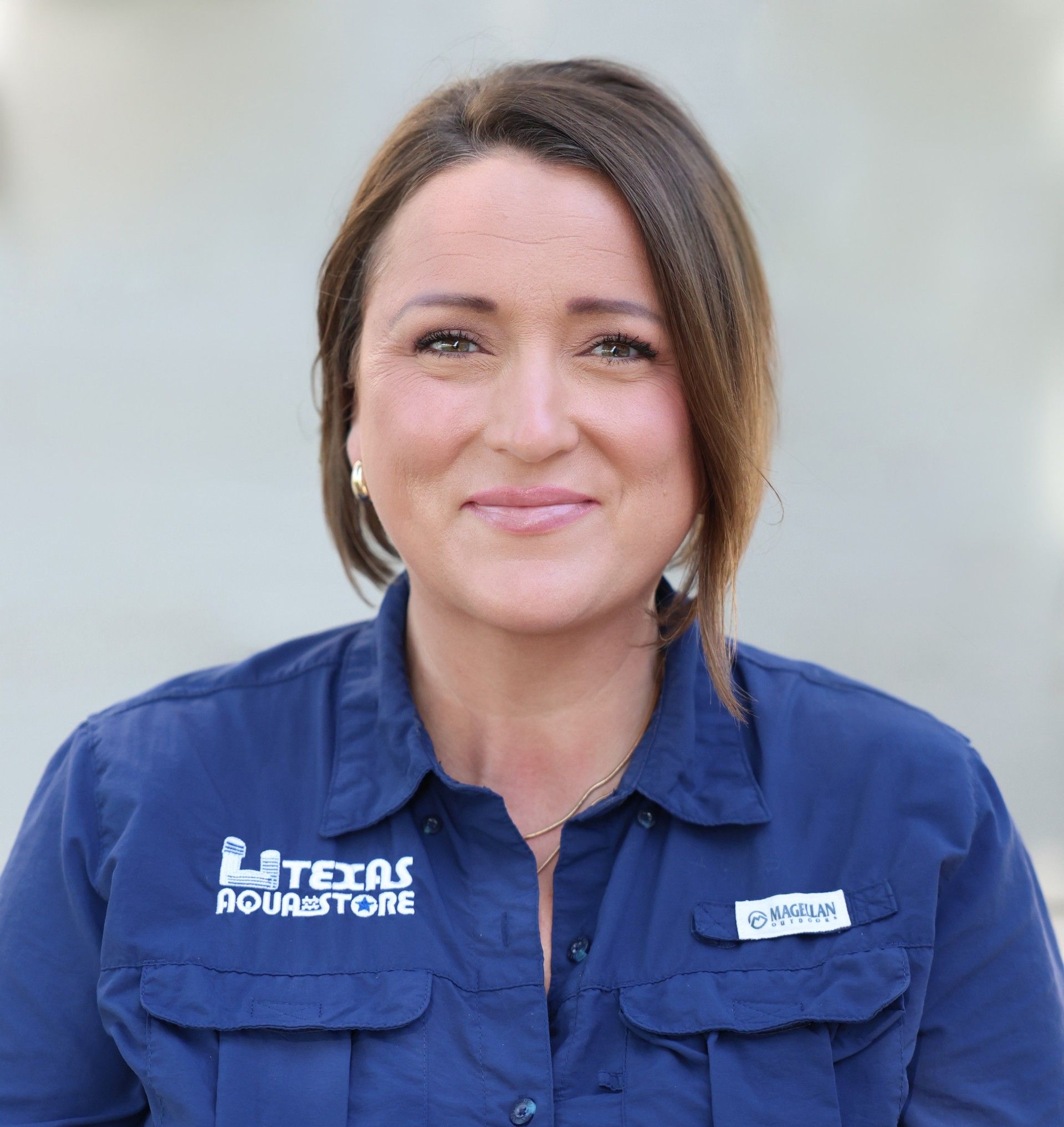 Man with a beard smiling, wearing a blazer over a patterned shirt, set against a light gray background.
