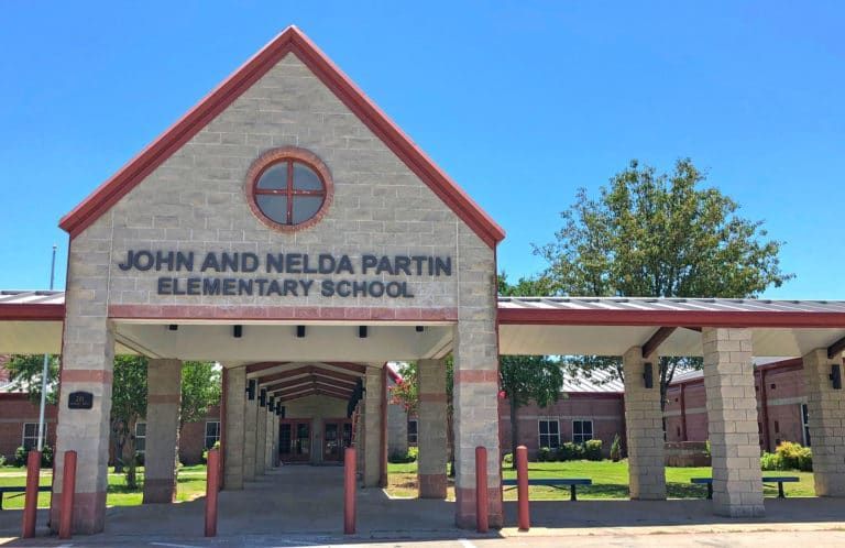 John and Nelda Partin Elementary School exterior; red-roofed entrance with text above, light brick walls, and sunny blue sky.