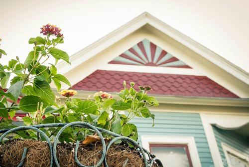 Close-up of a hanging flower basket in front of a house with a colorful roof and gable.