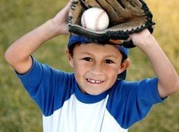 Young boy in blue baseball shirt holding a glove over his head, with a baseball inside, smiling.
