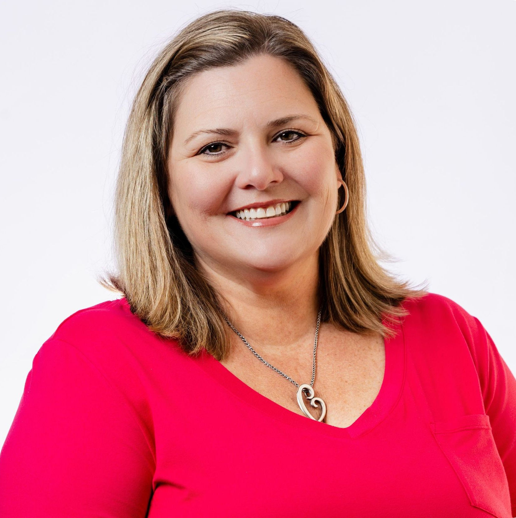 Man with a beard smiling, wearing a blazer over a patterned shirt, set against a light gray background.