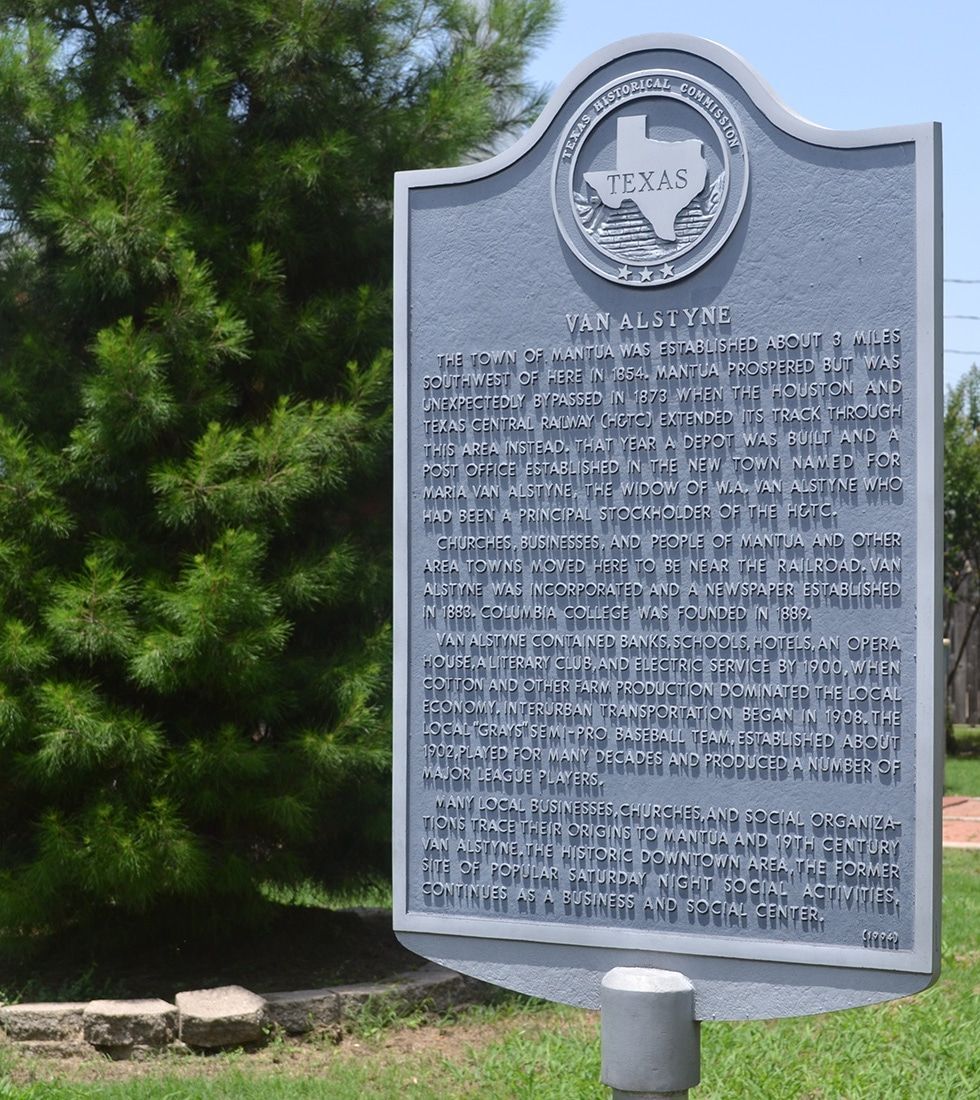 Texas historical marker with state seal, text on a gray plaque, set outdoors in front of a green tree.