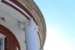 White Ionic column supporting a red brick and white facade with a clear blue sky in the background.