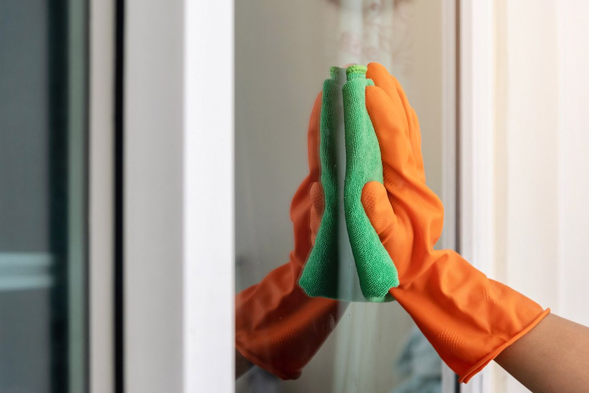A person wearing orange gloves is cleaning a window with a sponge