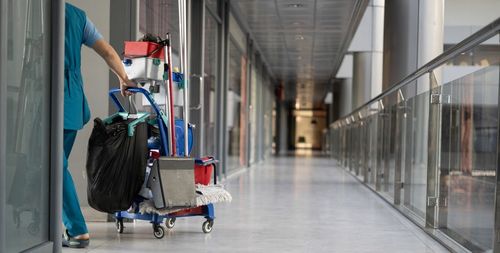 A woman is pushing a cleaning cart down a hallway