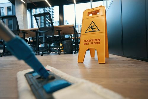 A mop is cleaning the floor in an office next to a caution wet floor sign