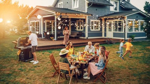 A group of people are sitting around a table eating food in front of a house.