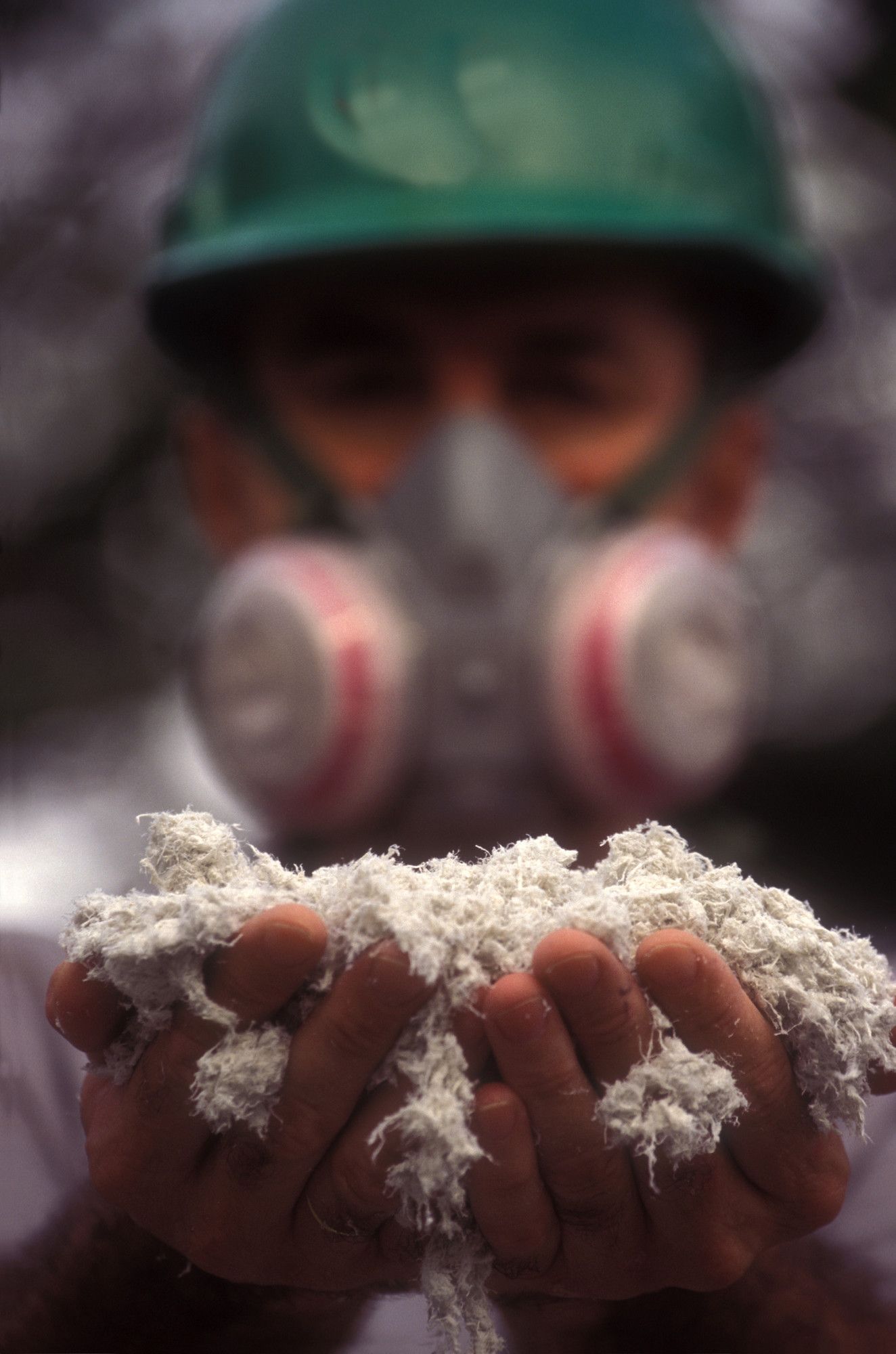 a man wearing a gas mask is holding a pile of asbestos in his hands