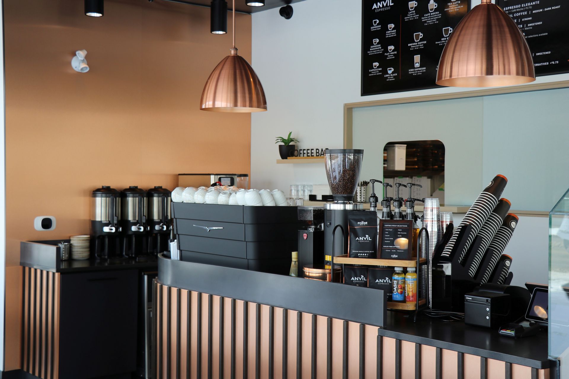 The Forge shop counter with espresso machine, grinder, and cups. Copper light fixture and brown walls.