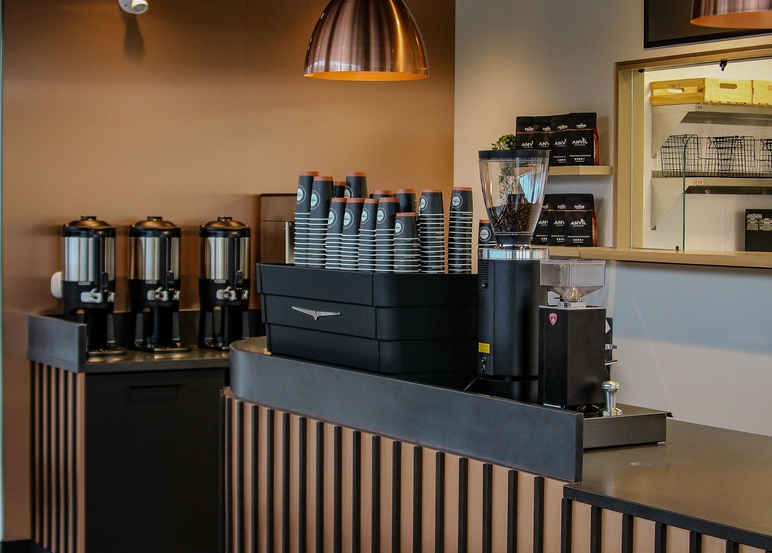 The Forge shop counter with espresso machine, grinder, and cups. Copper light fixture and brown walls.