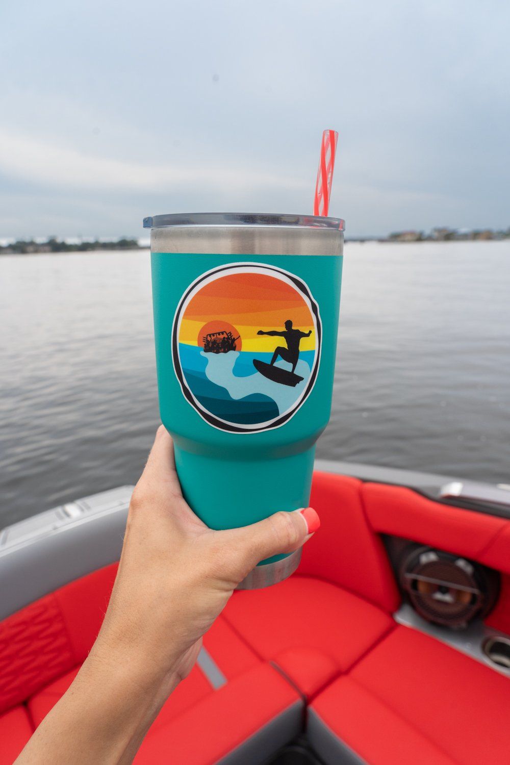 A person is holding a cup with a surfer on it in front of a boat.