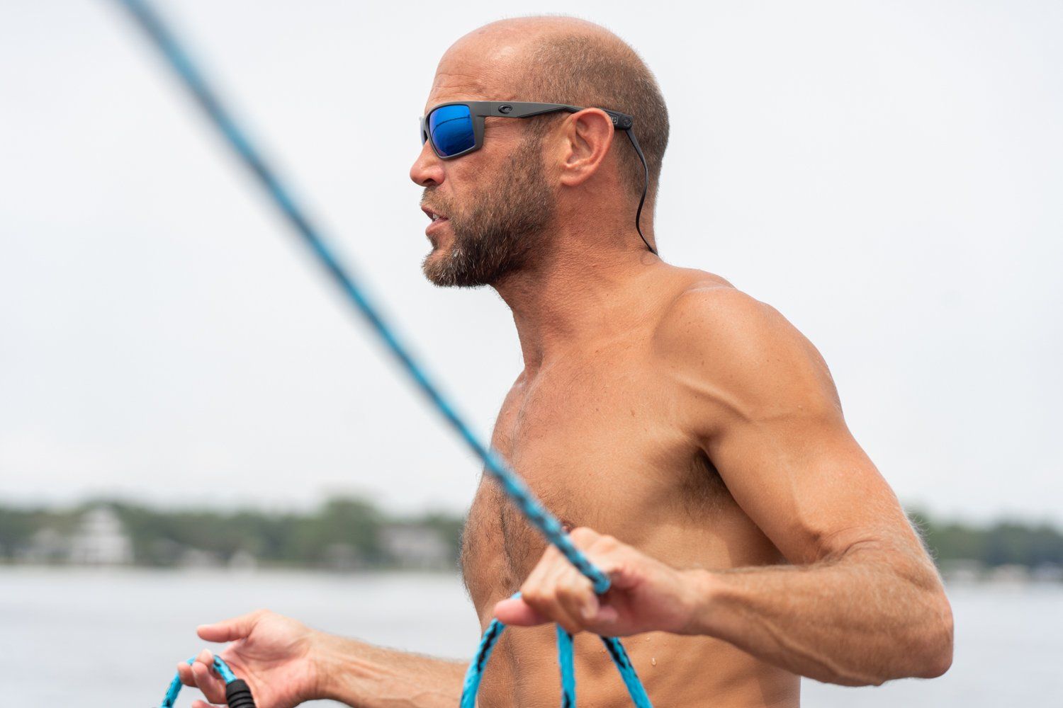 A shirtless man wearing sunglasses is holding a blue rope.