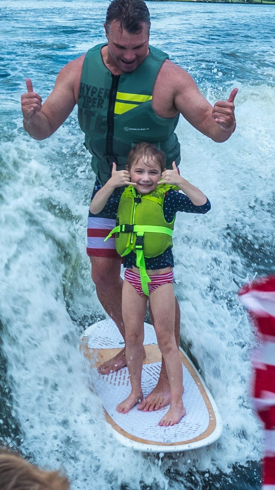A man and a little girl are riding a surfboard in the water.