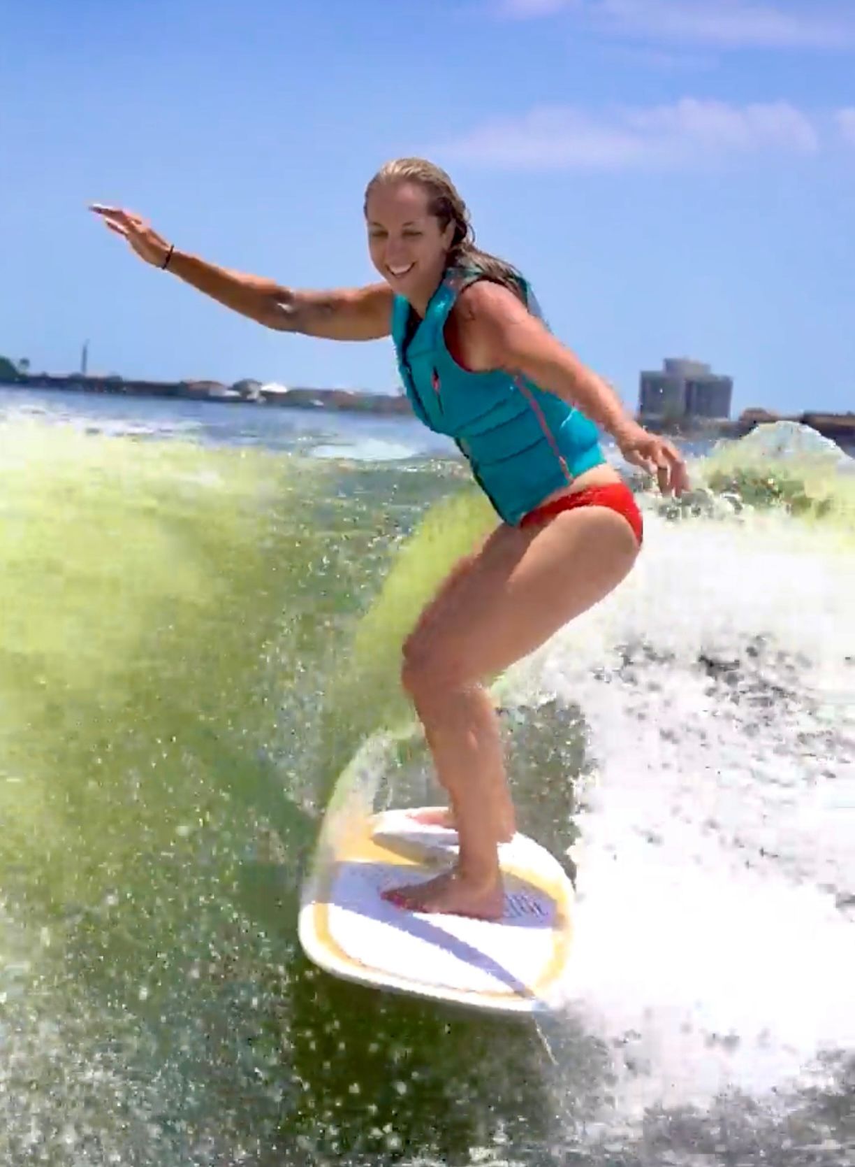 A woman in a blue vest is riding a wave on a surfboard