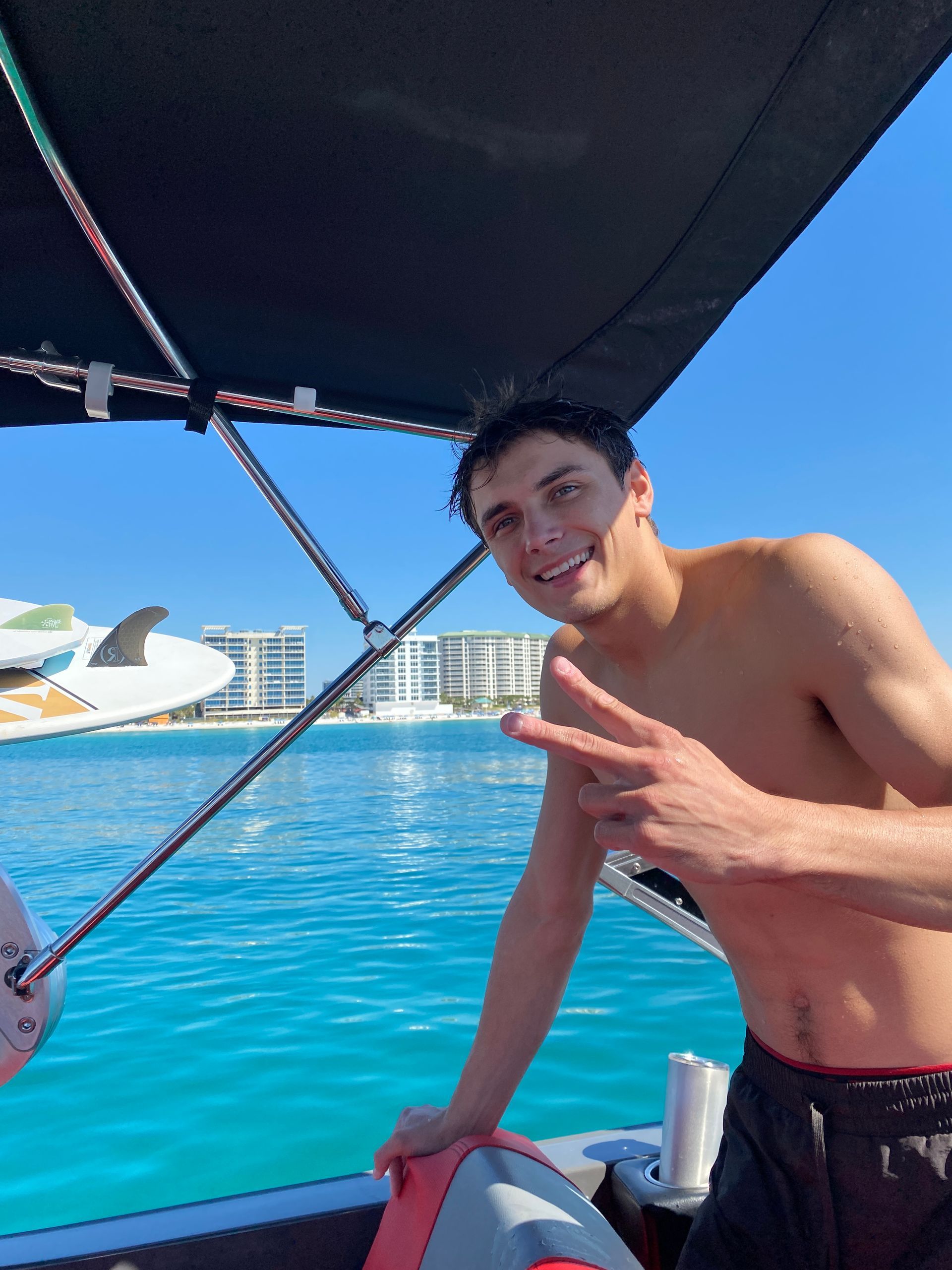 A shirtless man on a boat giving a peace sign