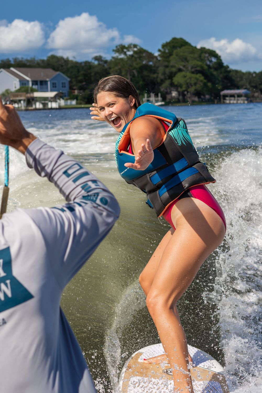 A woman in a life jacket is riding a wakeboard on a lake.