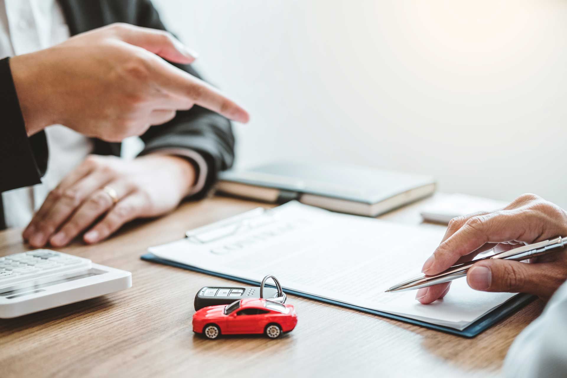 Person pointing at document as another person signs, car keys and toy car on desk.