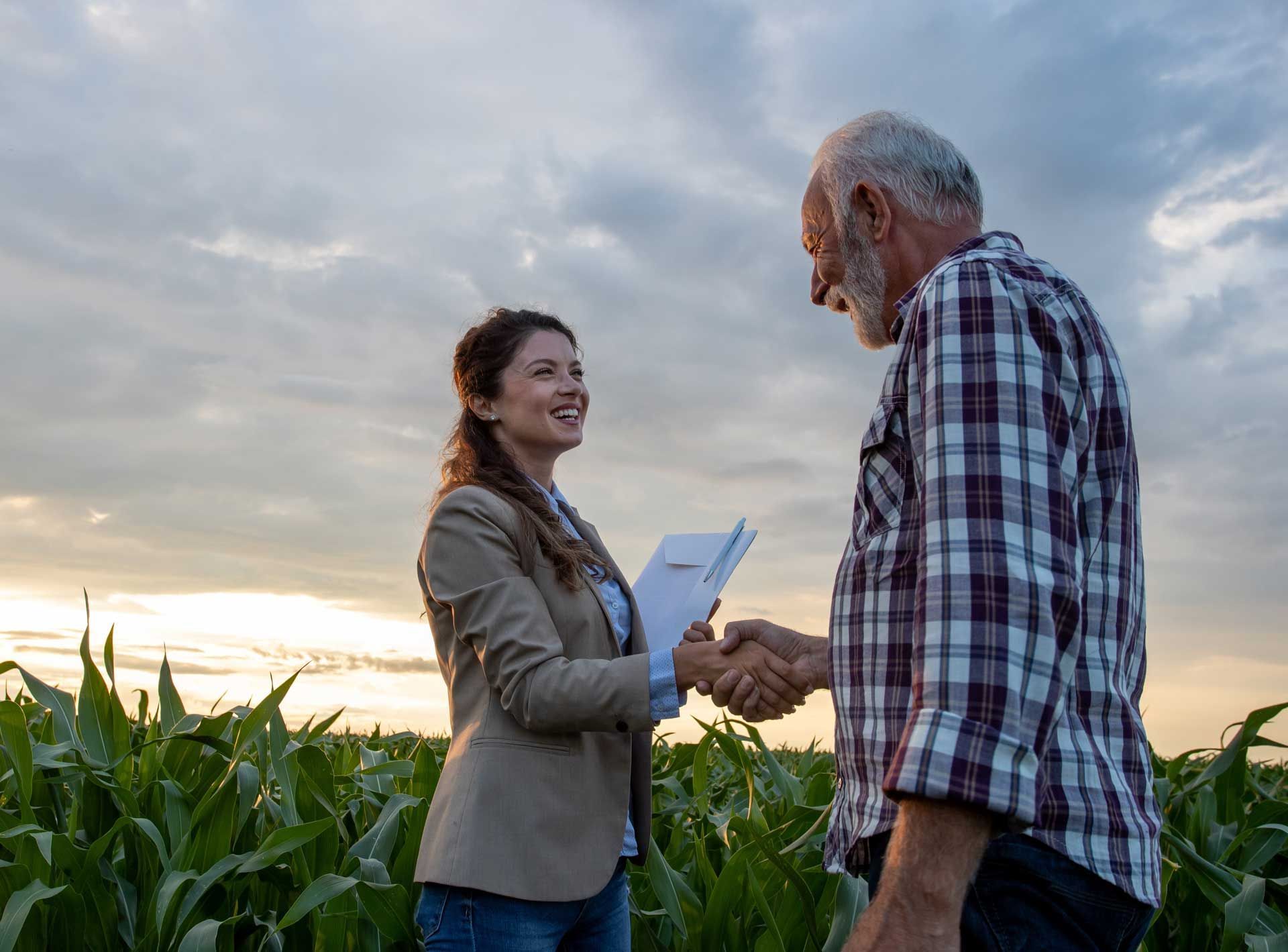 Woman in suit shaking hands with a farmer in a field; sky background. Woman in suit shaking hands with a farmer in a field; sky background.