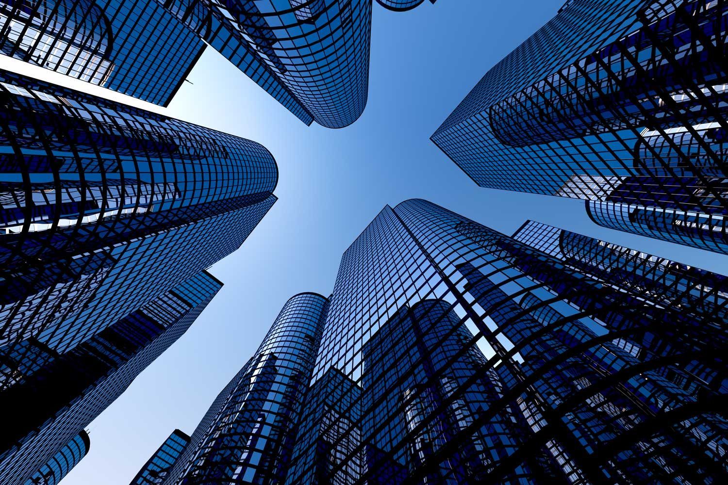 Low-angle shot of tall skyscrapers reaching towards a clear blue sky; glass facades reflect sunlight.